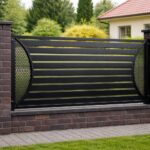 Modern black metal privacy fence panel with horizontal slats and decorative curved perforated side details mounted between dark brick pillars.