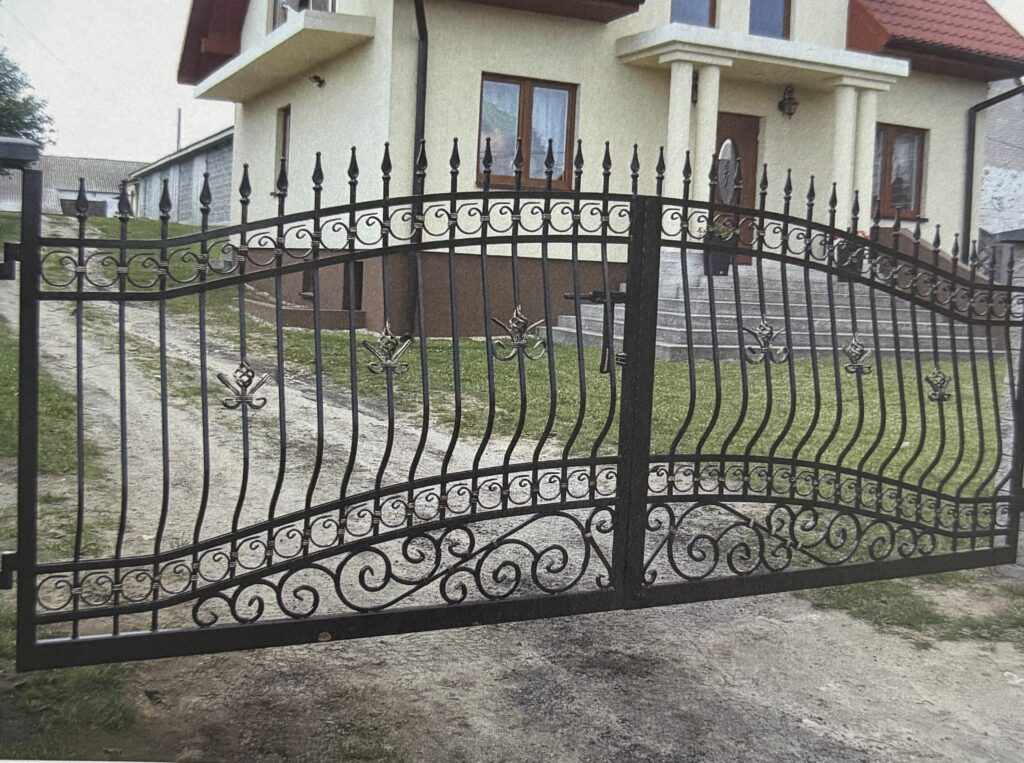 Decorative wrought iron driveway gate with ornamental scrollwork installed at a residential property.
